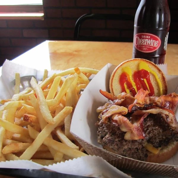 A bacon cheeseburger with fries and a Cheerwine bottle on a wooden table.