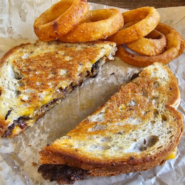 A grilled cheese sandwich cut in half, revealing melted cheese and meat, served with onion rings.