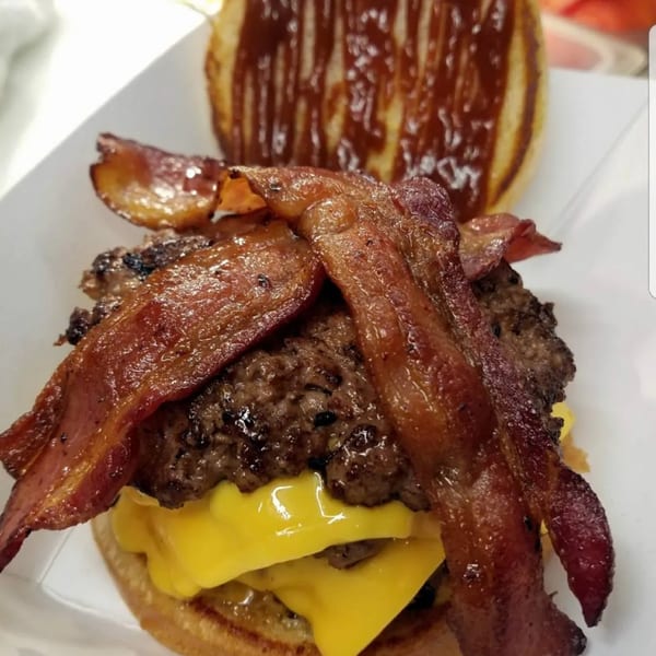 Close-up of a Paige's Root Beer bacon cheeseburger with melted cheese and barbecue sauce on the bun.