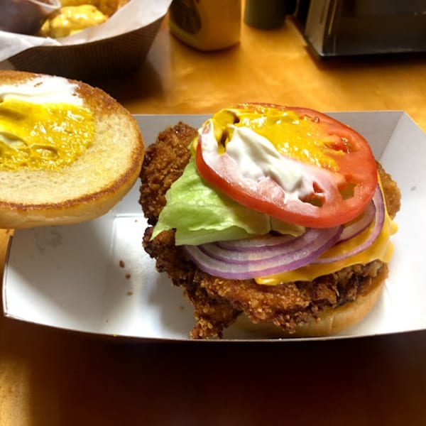 A crispy fried chicken sandwich with lettuce, red onion, cheese, tomato, mustard, and mayonnaise.