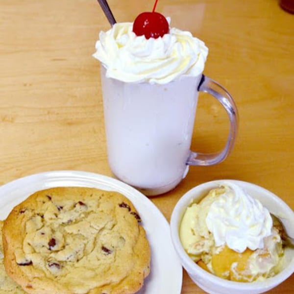 A Paige's Root Beer milkshake with a cherry, a chocolate chip cookie, and a bowl of banana pudding.