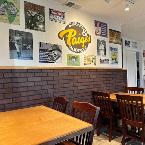 Interior of Paige's Root Beer with wooden tables, chairs, brick wainscoting, and vintage posters on the wall.