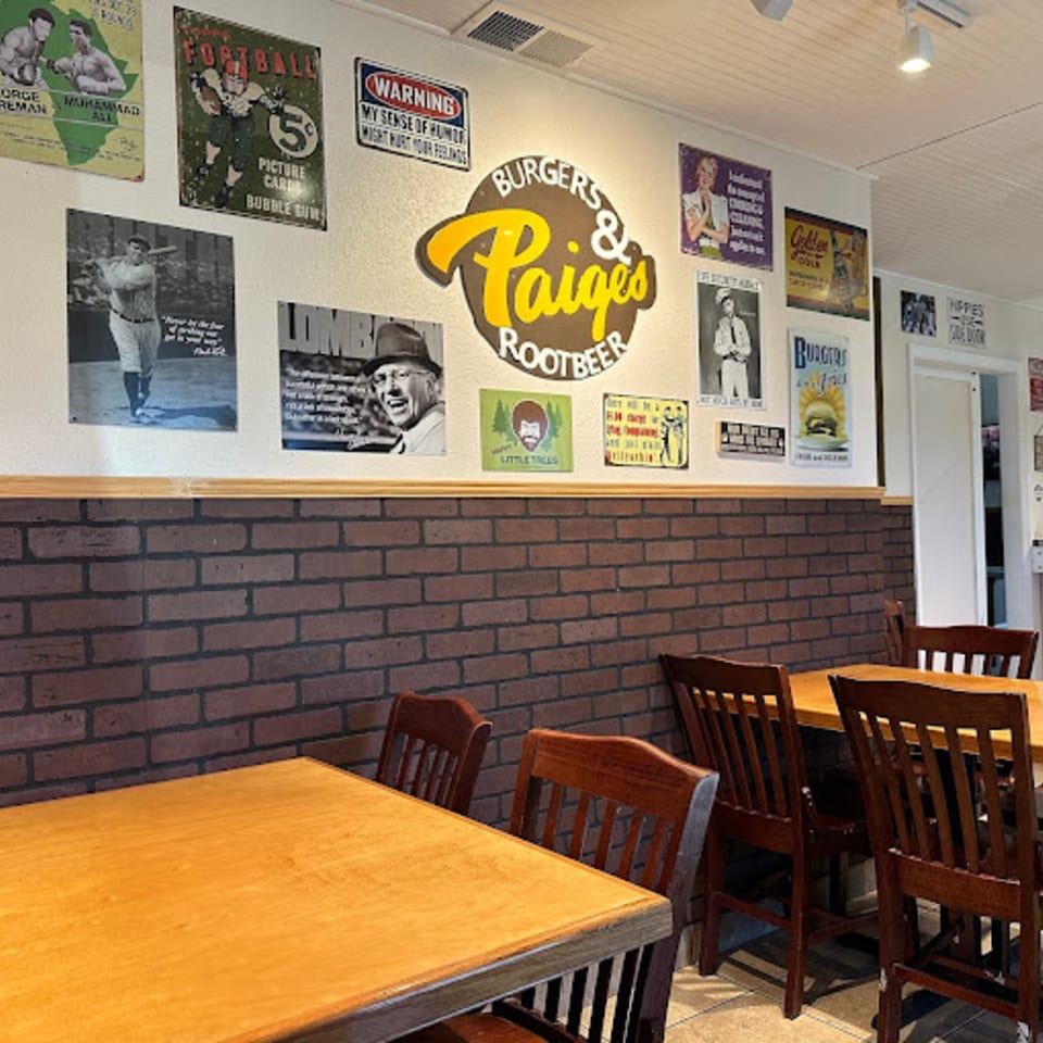 Interior of Paige's Root Beer with wooden tables, chairs, brick wainscoting, and vintage posters on the wall.